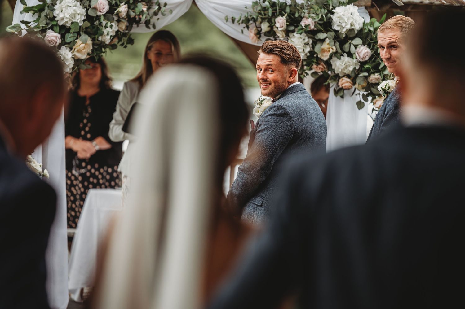A happy moment captured during a wedding ceremony under a floral arch with white roses and greenery.