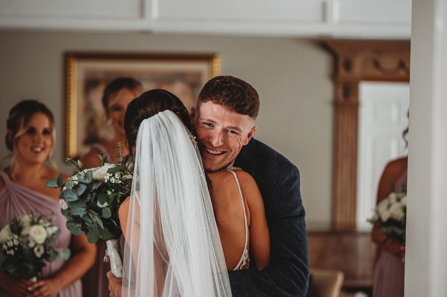 An intimate moment between a couple at their wedding ceremony, with bridesmaids and floral decorations visible in the background.