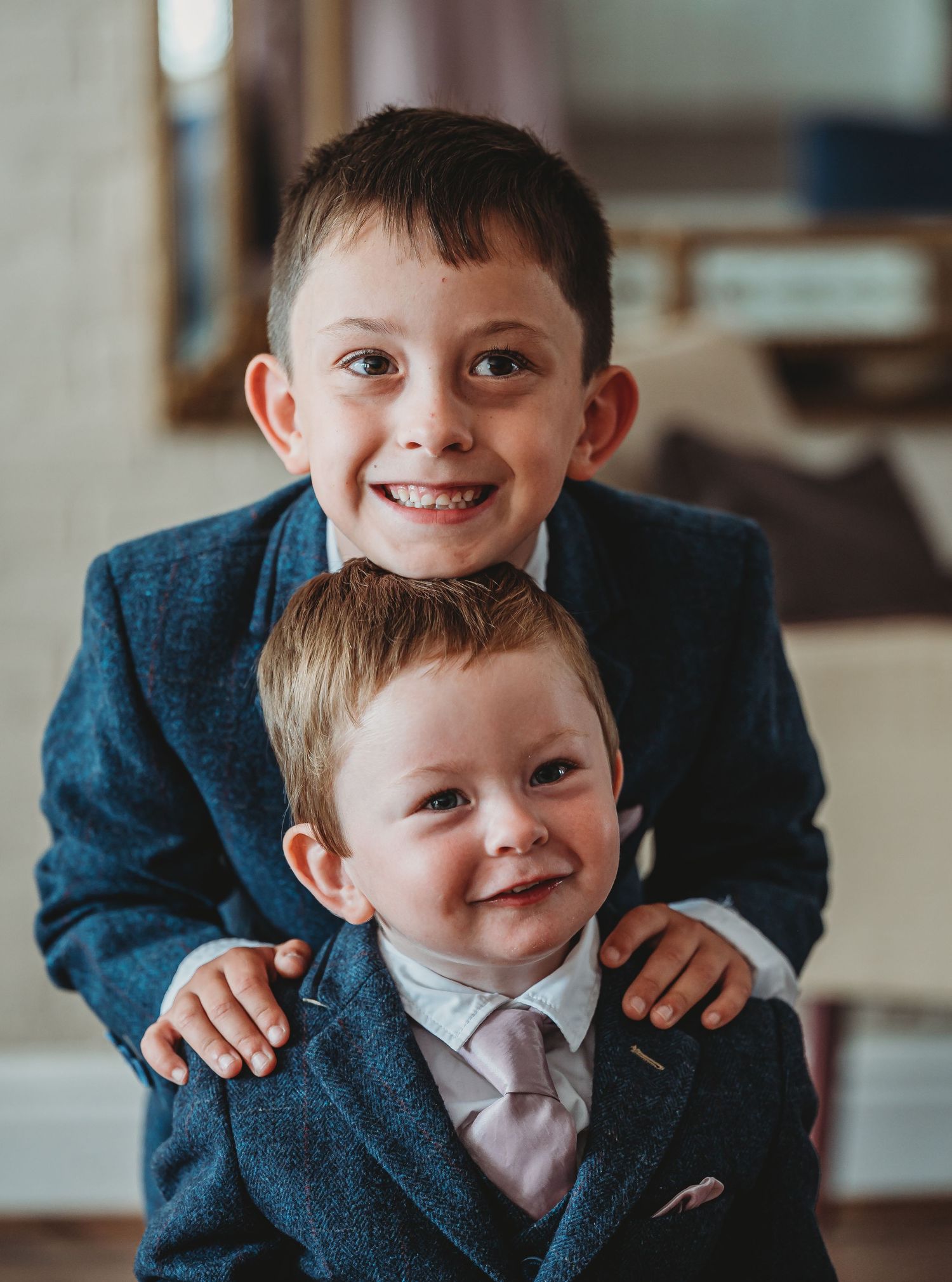 Two young brothers in matching navy suits and ties share a heartwarming moment together while smiling at the camera.