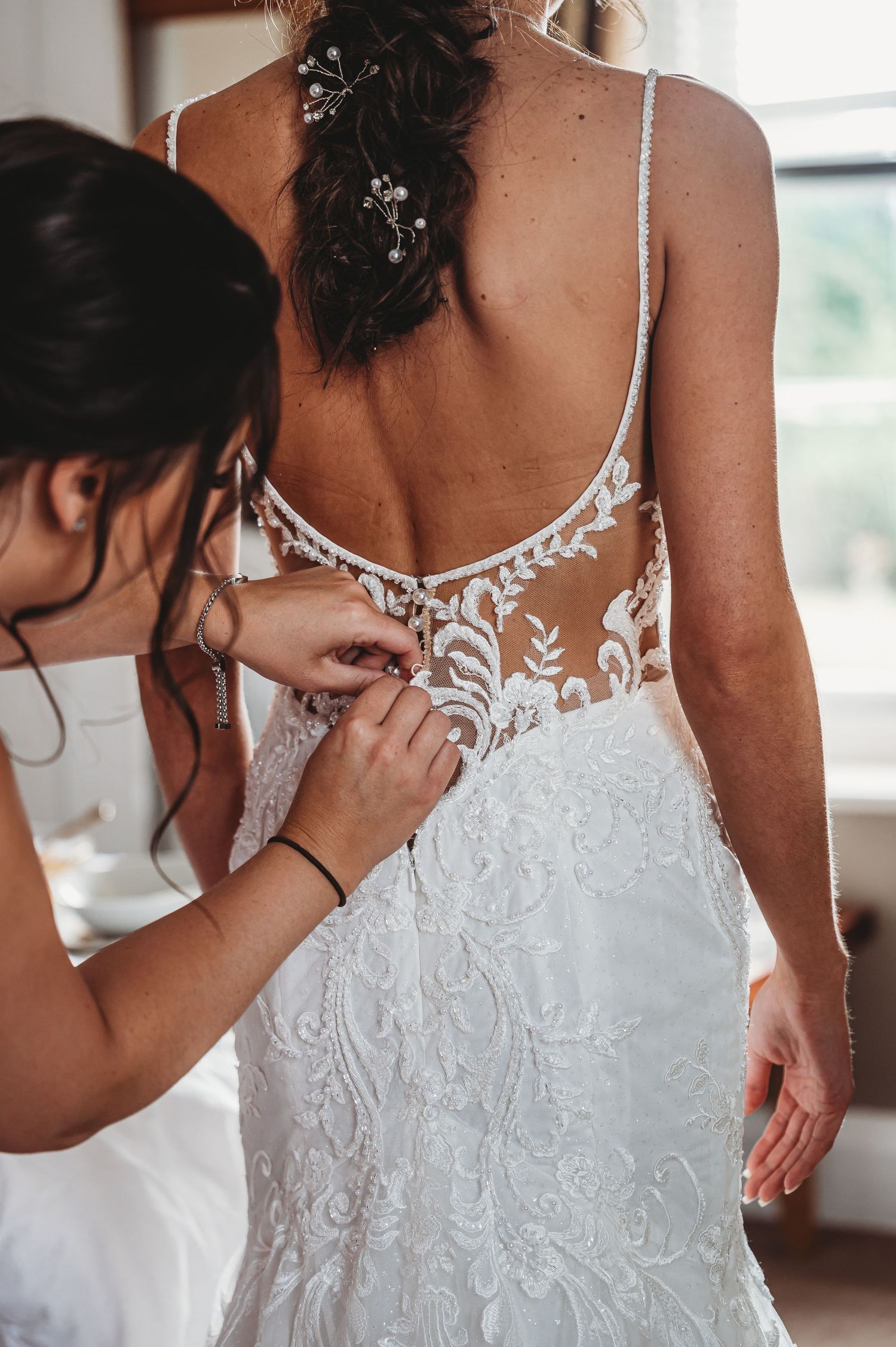 A wedding dress being adjusted, showing intricate white lace details and floral embroidery on the back.