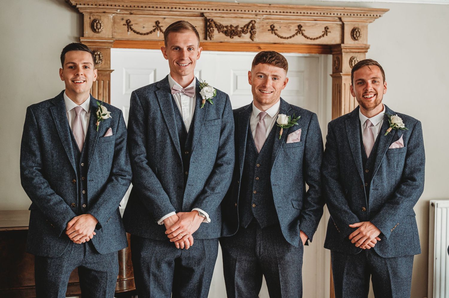 A group of groomsmen in matching navy blue suits with light floral boutonnieres stand together at a wedding.