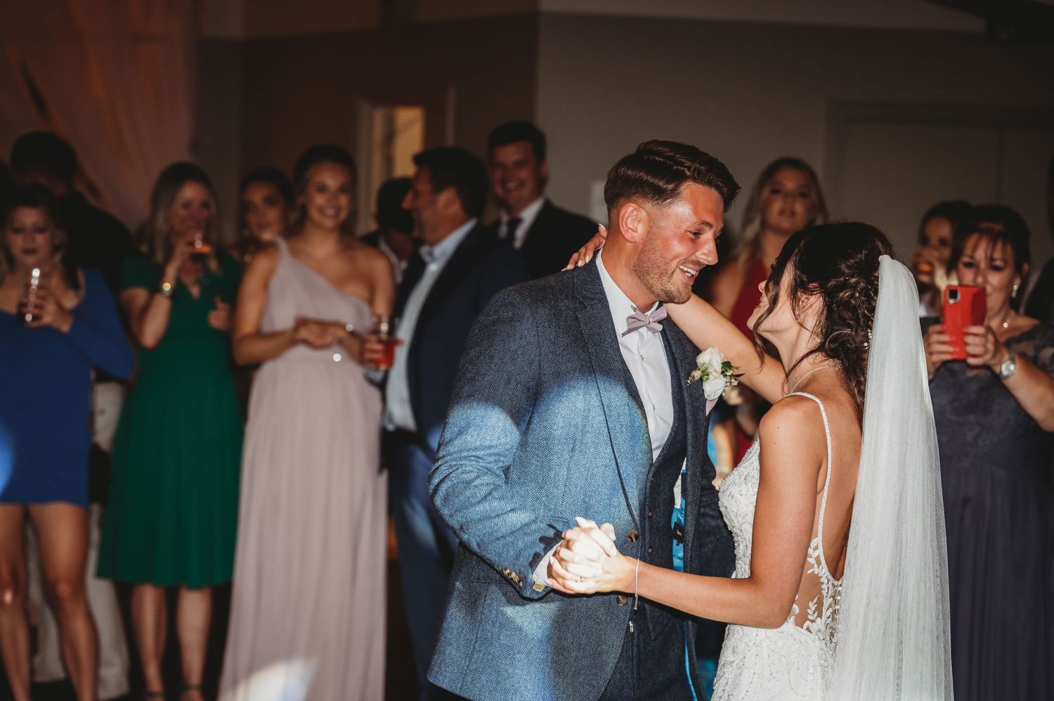 A bride and groom share their first dance at a wedding reception while guests watch in the background.