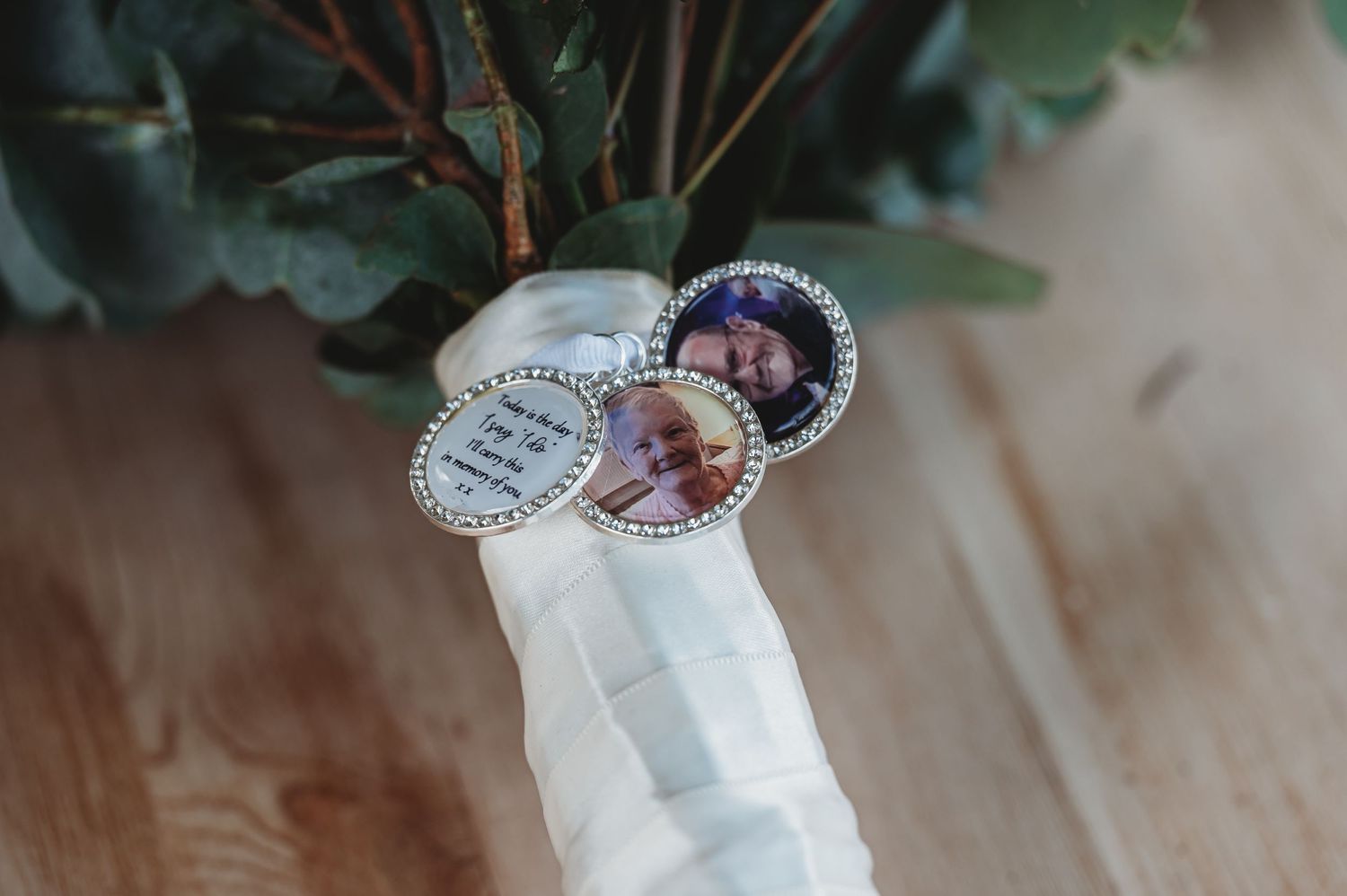 Custom photo pins or buttons attached to white fabric near green foliage on a wooden surface.