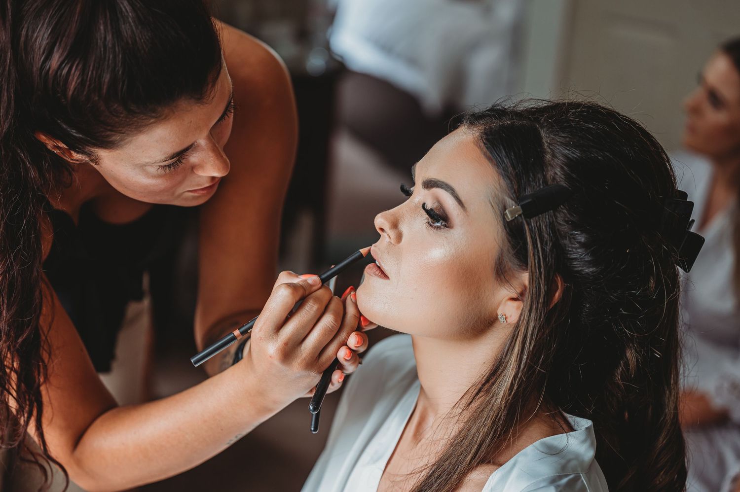 Makeup artist applies lipstick to client during bridal beauty preparation session.