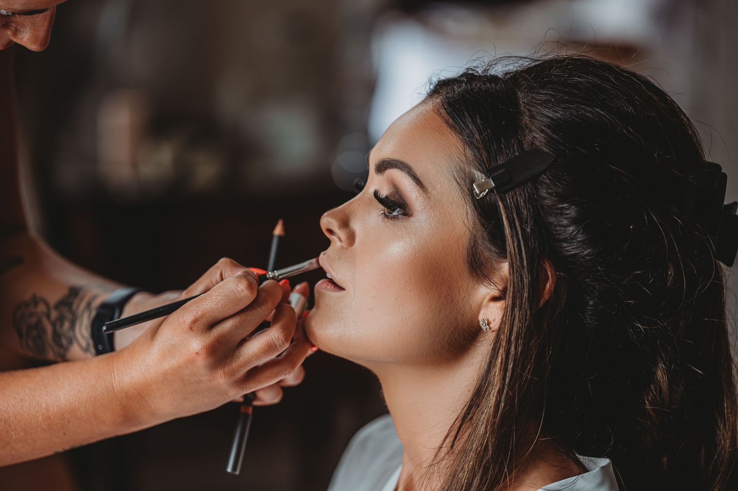 Professional makeup artist applying lipstick on a client during a beauty session in warm lighting.