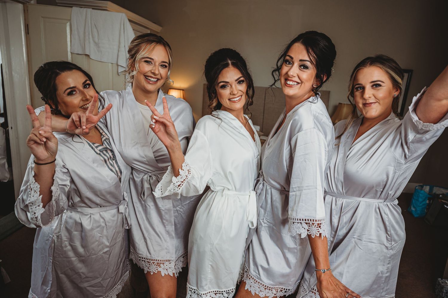 A group of five people wearing matching white robes pose together and smile for a bridal preparation photo.