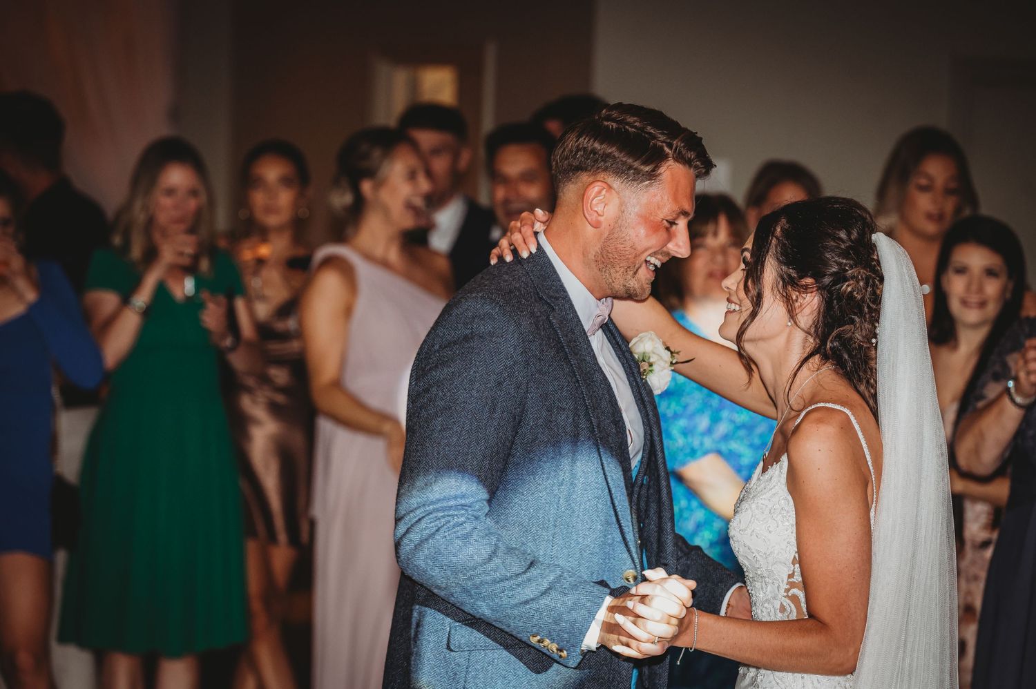 Newlyweds share an intimate first dance while wedding guests watch and cheer in the background.