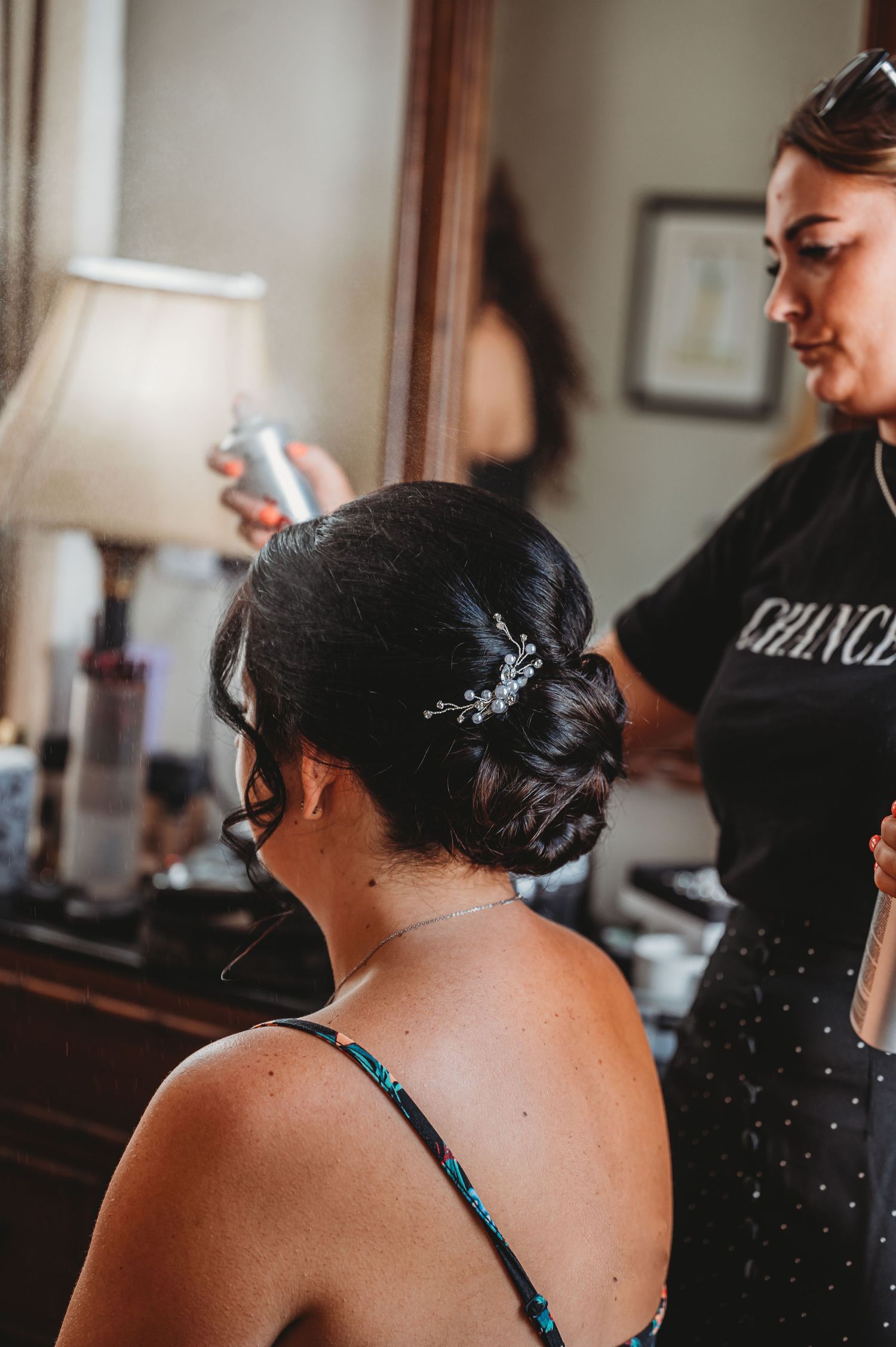 A hairstylist applies finishing touches to an elegant updo with a delicate crystal hair accessory.