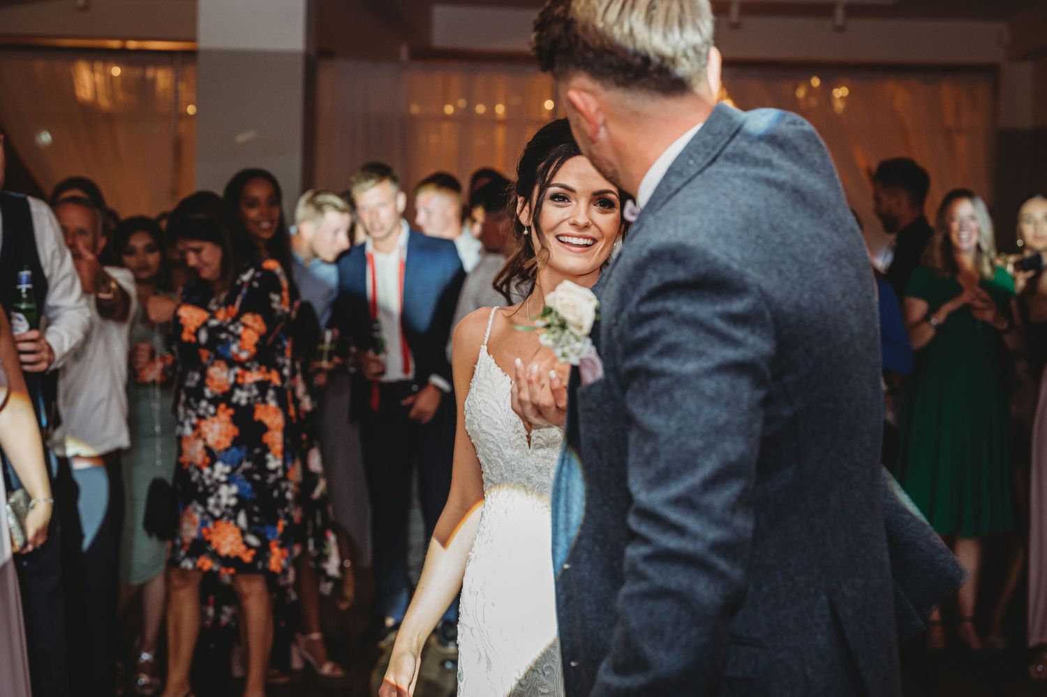 A couple shares their first dance at a wedding reception while guests watch and take photos in the background.