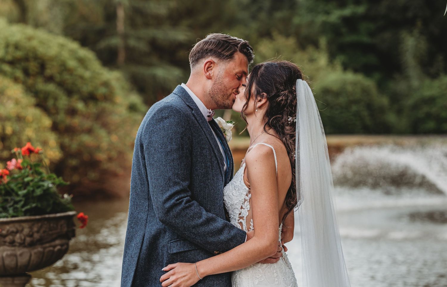 A romantic wedding moment captured outdoors with a flowing veil and lush greenery in the background.