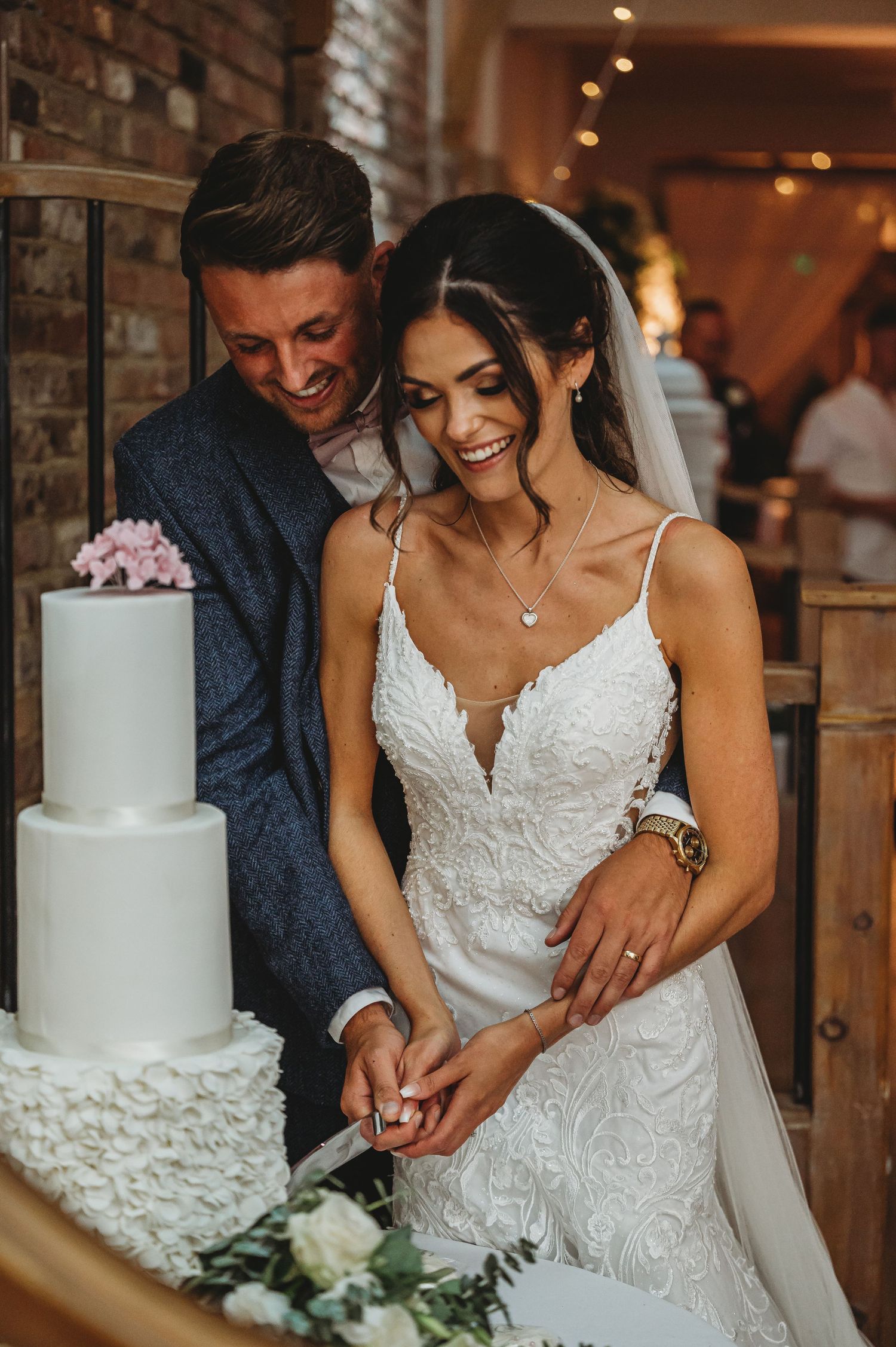 A bride and groom share a joyful moment while cutting their elegant white wedding cake at their reception.