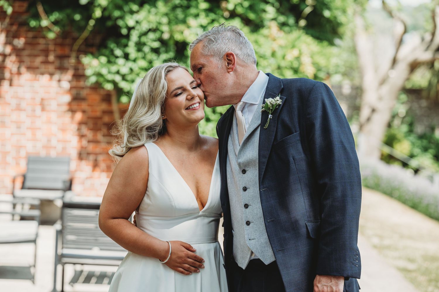 A couple shares a joyful moment together outdoors on their wedding day at a venue with a brick wall backdrop.