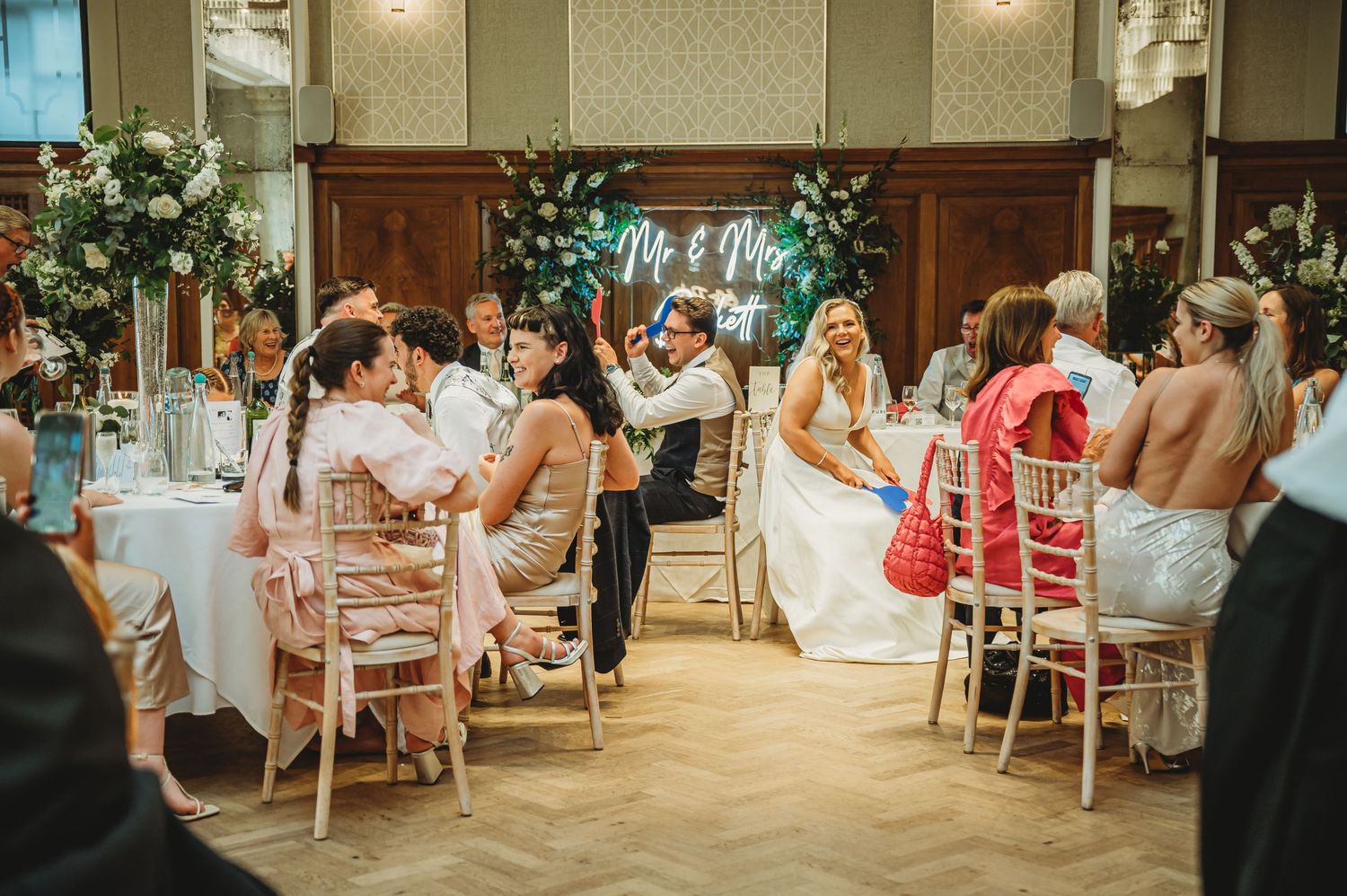 Elegant wedding reception hall with guests dining at round tables.