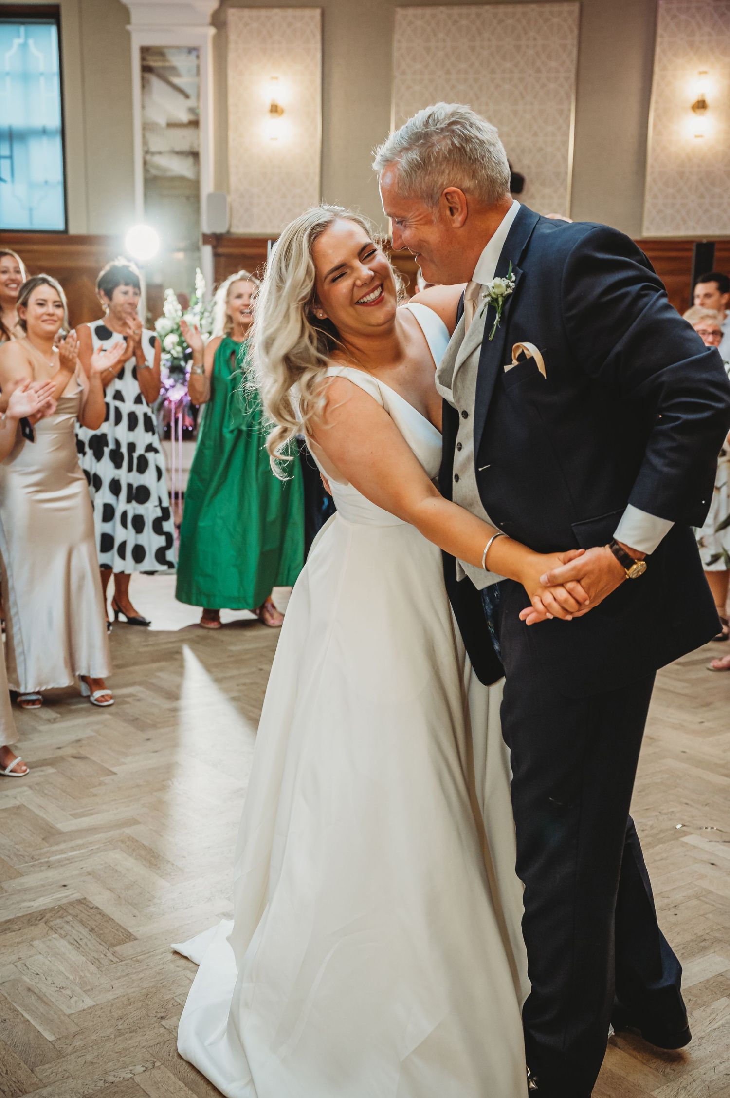Wedding couple shares a joyful dance moment on the reception floor as guests in formal attire look on and celebrate.