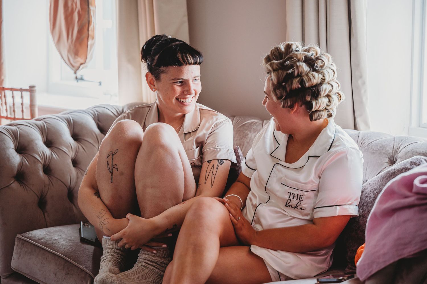 Two people sitting close together on a gray tufted couch share a casual conversation.