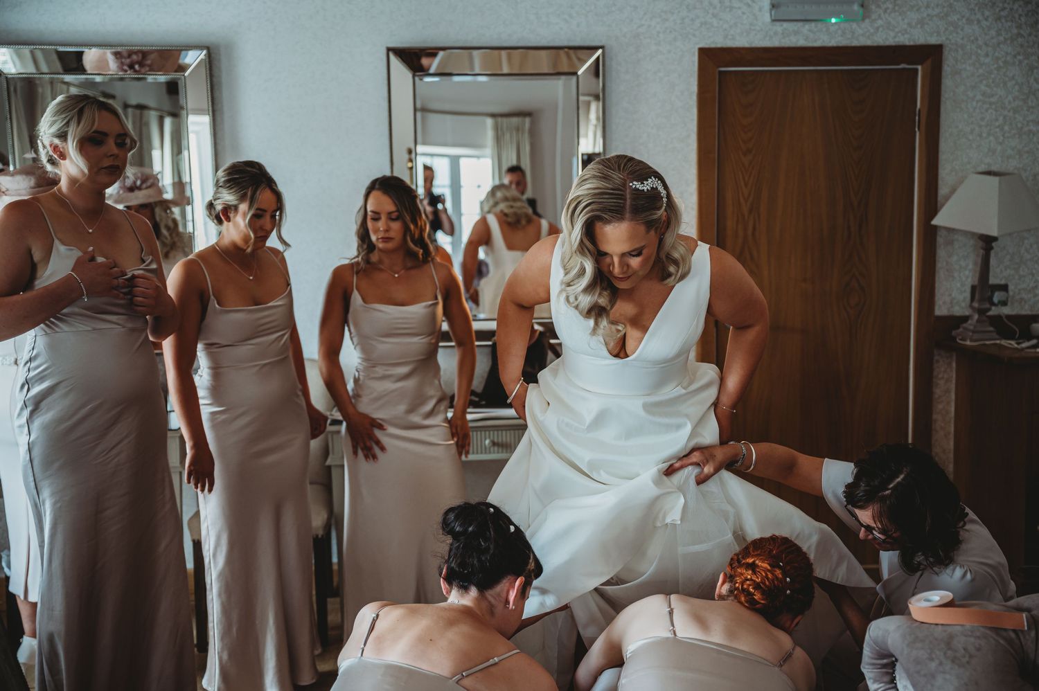 Wedding party in light colored dresses helps prepare for the ceremony in a dressing room.