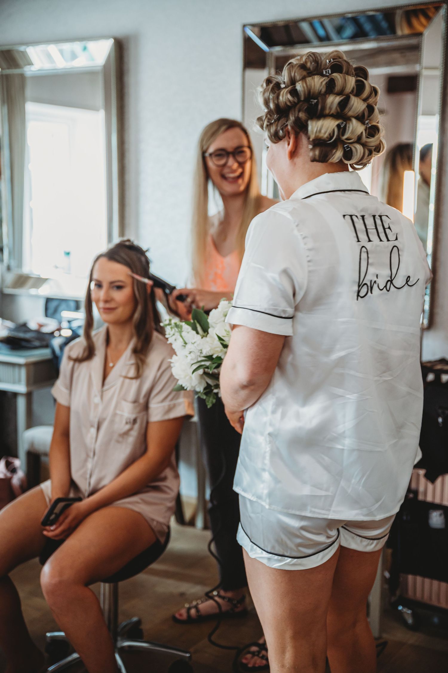 Wedding morning preparations show hair and makeup session with bride and bridesmaids in casual getting-ready attire.