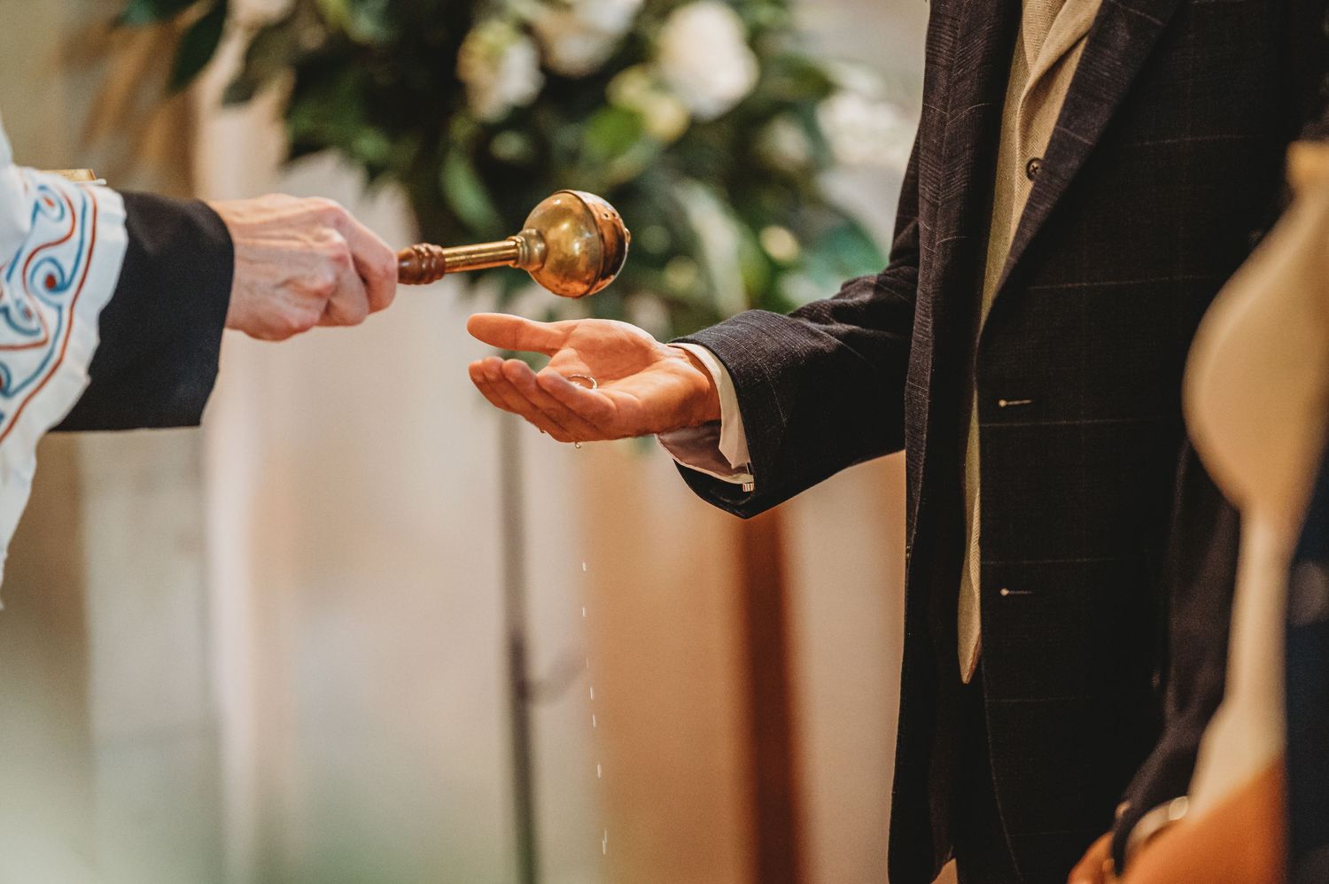 Close-up shot of a wedding ring exchange ceremony with hands passing a gold ring in warm lighting.