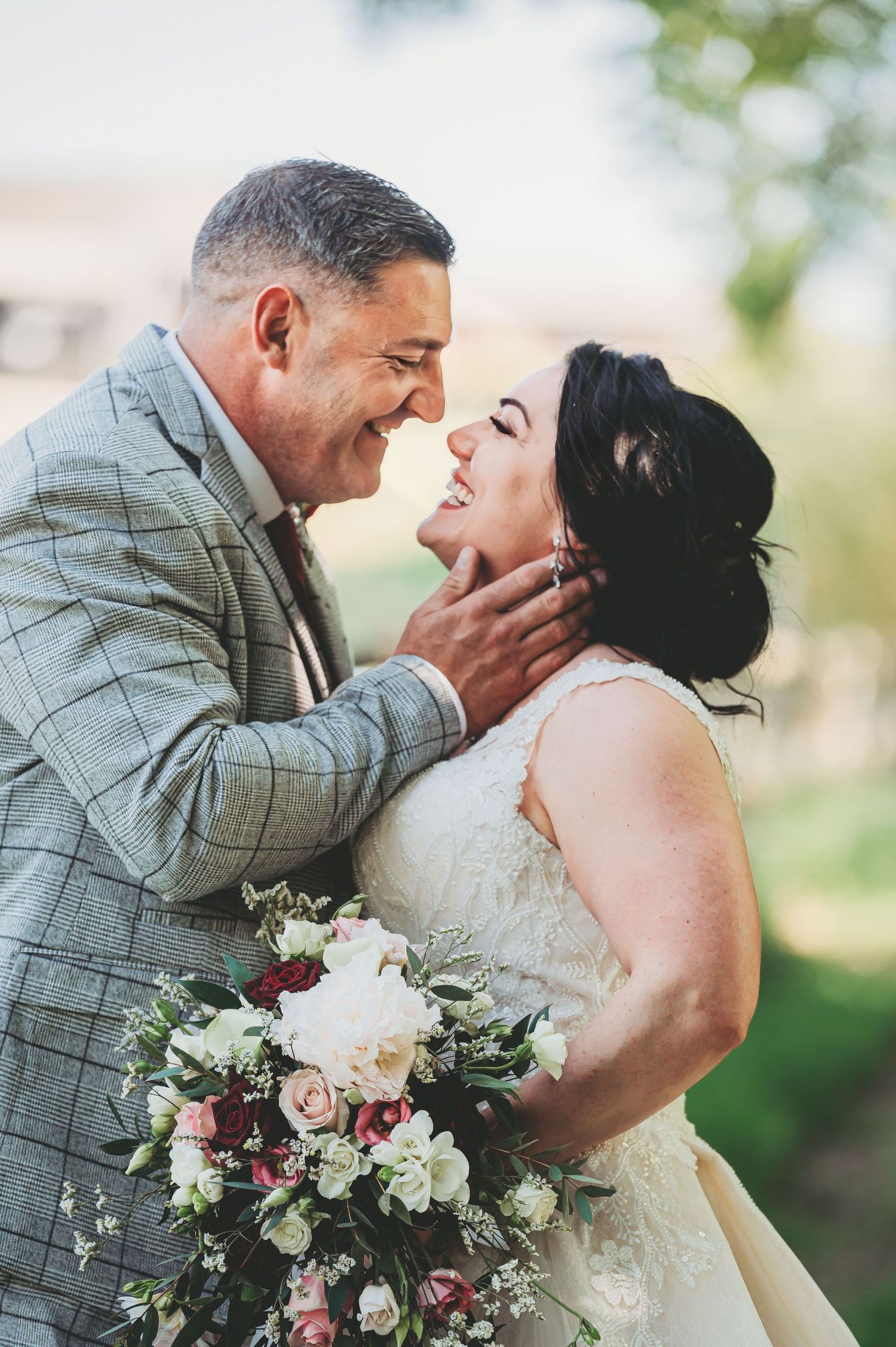 Joyful couple shares an intimate moment while the bride holds a beautiful bouquet of pink and white flowers.