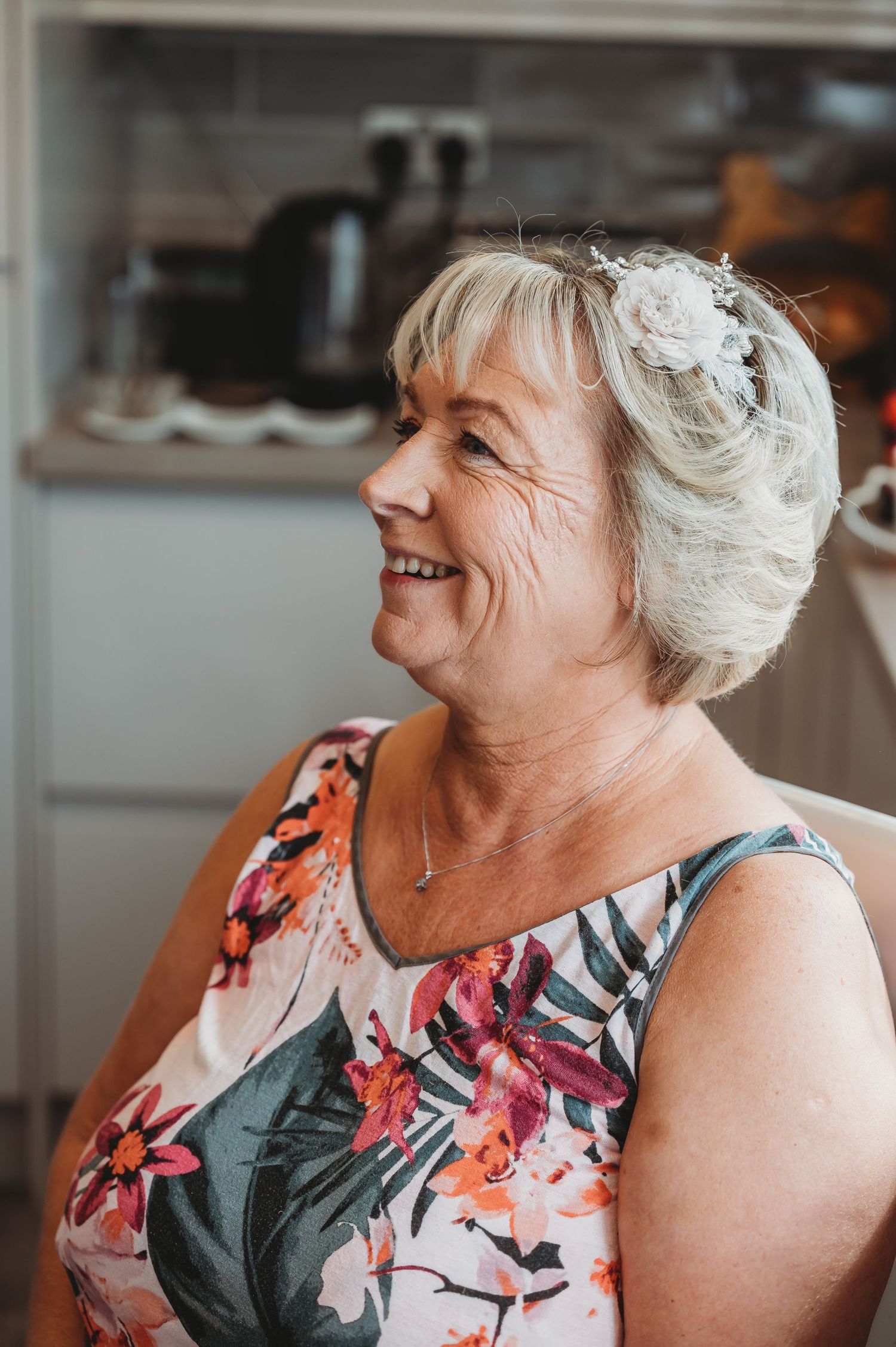 A side profile portrait shows a woman in a floral sleeveless dress smiling warmly against a blurred kitchen background.