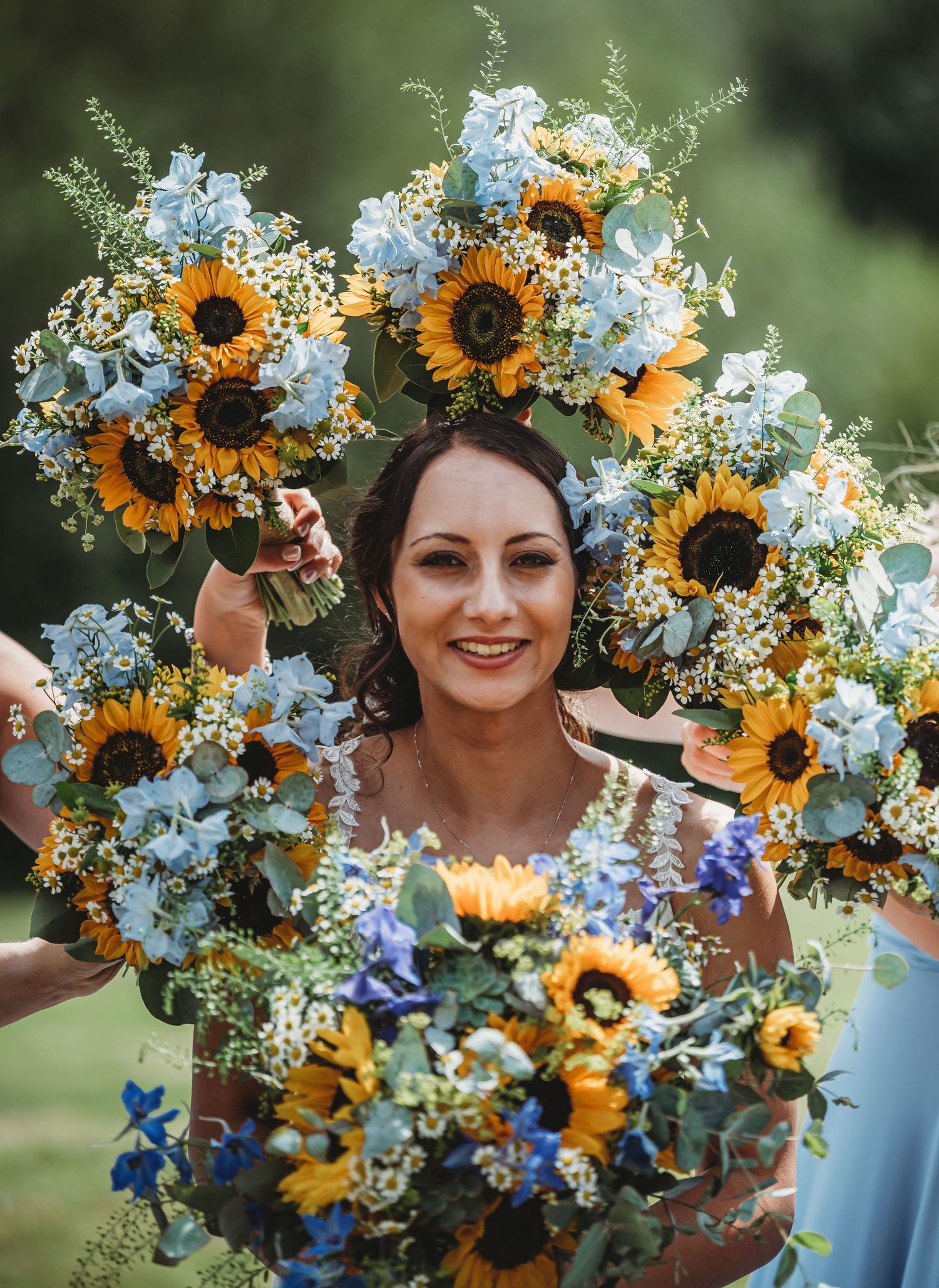 Beautiful wedding bouquets featuring vibrant sunflowers and light blue delphinium flowers arranged in a rustic garden style.