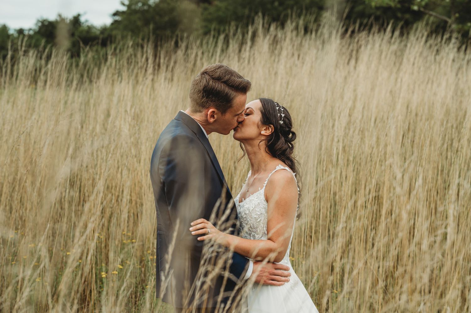 A couple embraces tenderly among tall golden prairie grass during a romantic outdoor photoshoot.