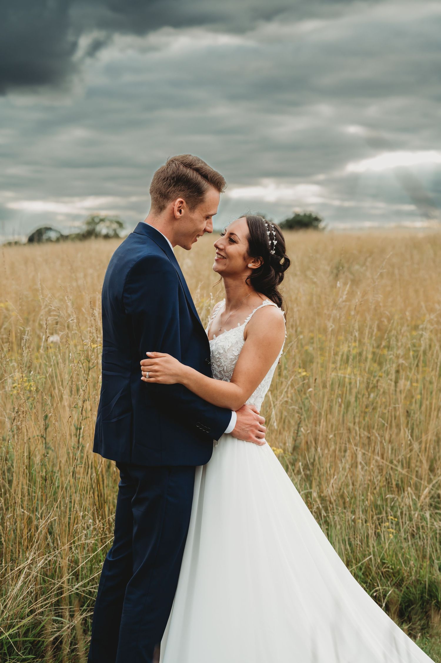 A romantic wedding portrait captured in a golden wheat field under dramatic stormy clouds.