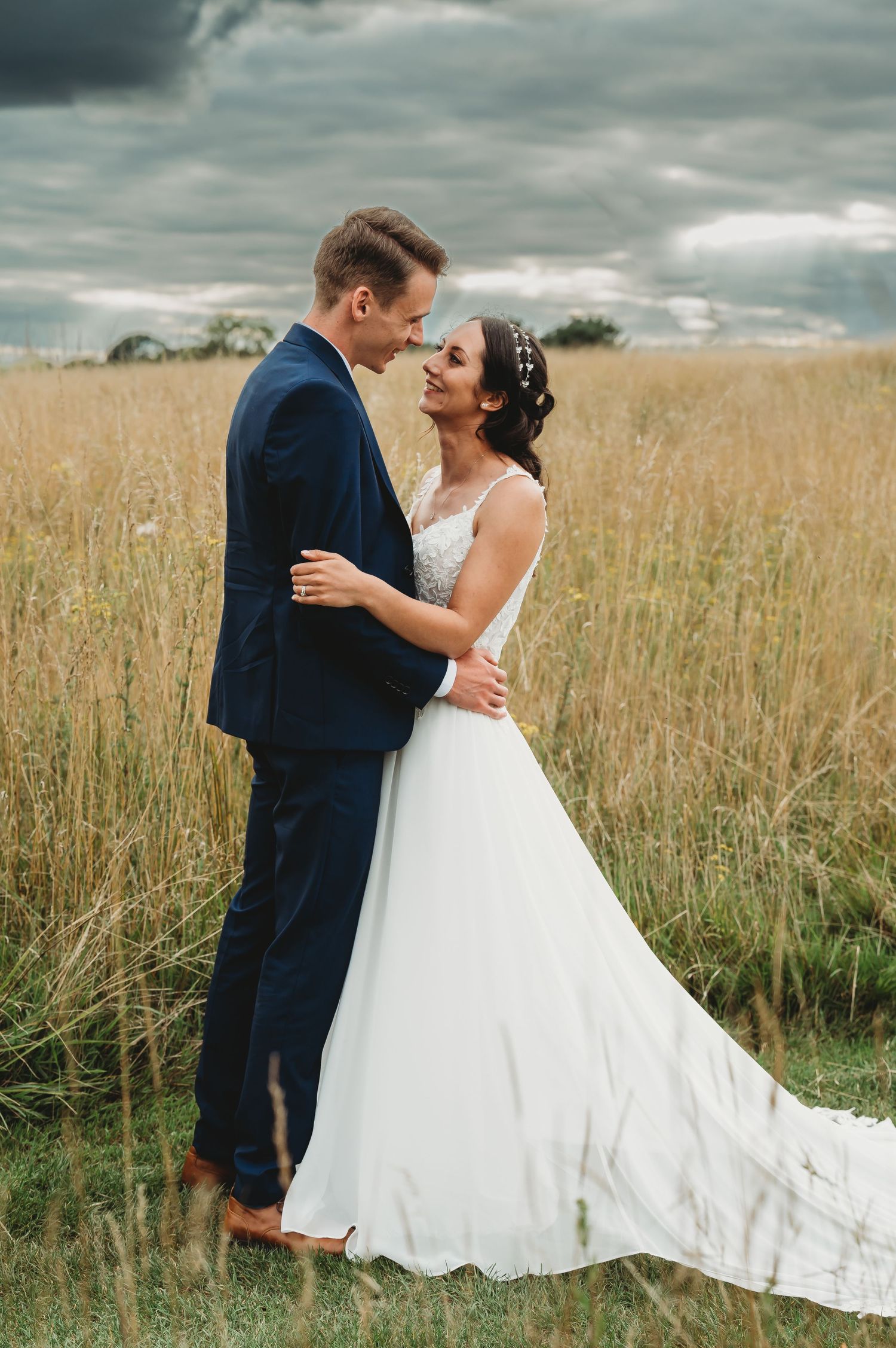 A couple embraces in a golden wheat field during their wedding photoshoot under stormy skies.