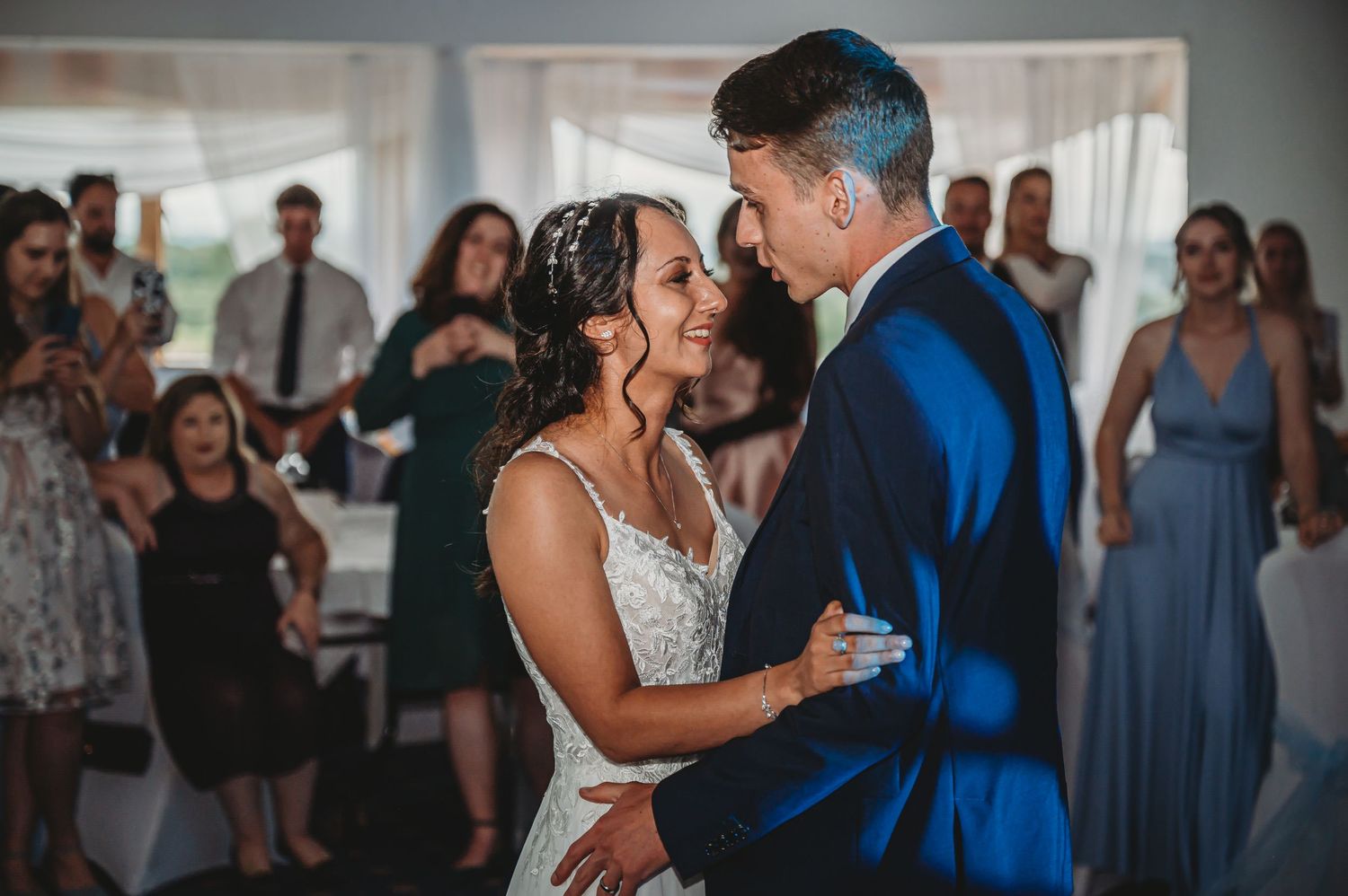 A couple shares their first dance as newlyweds at a wedding reception while guests look on in the background.