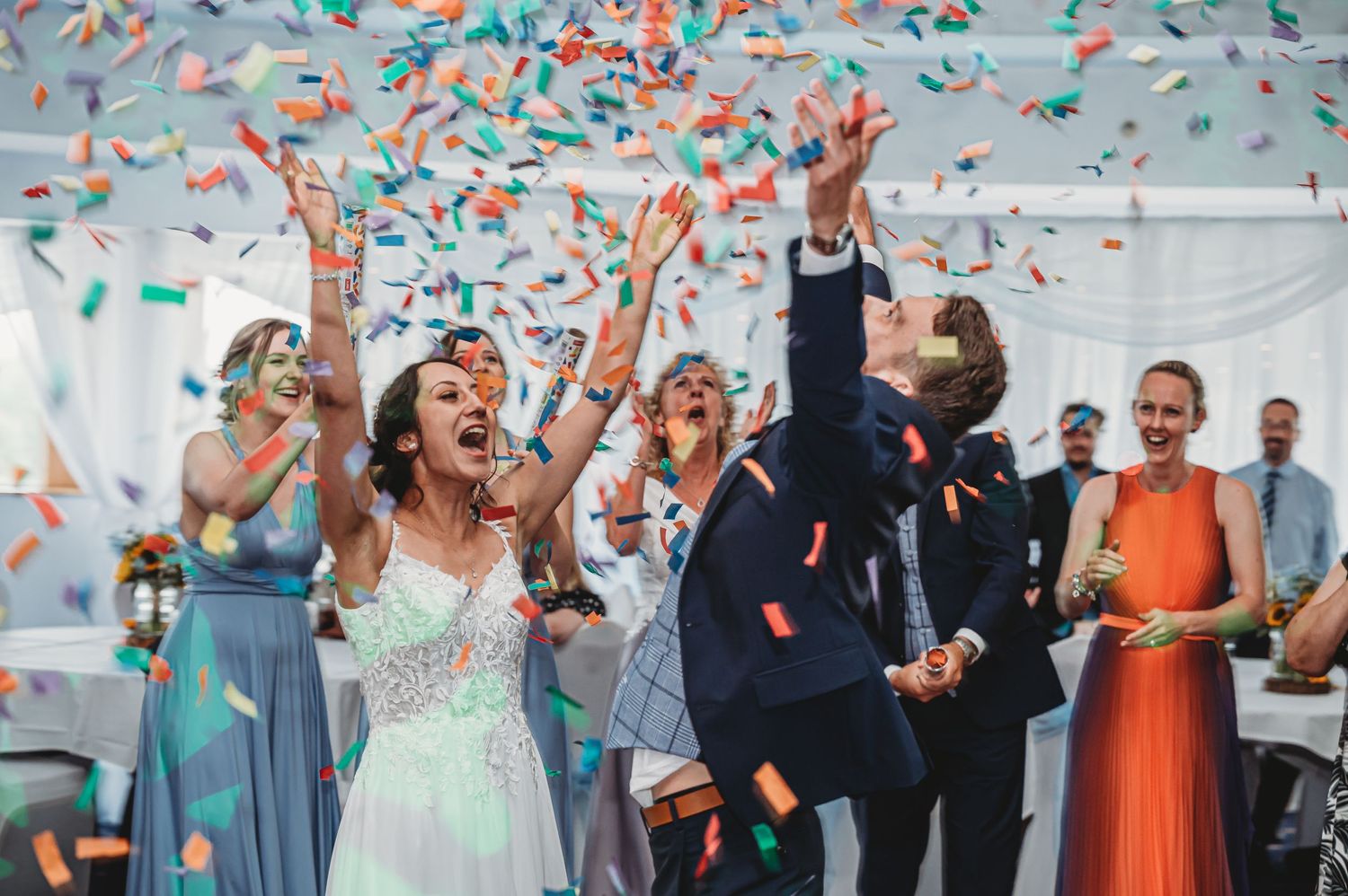 Wedding celebration with guests showered in colorful confetti during joyous reception moment.