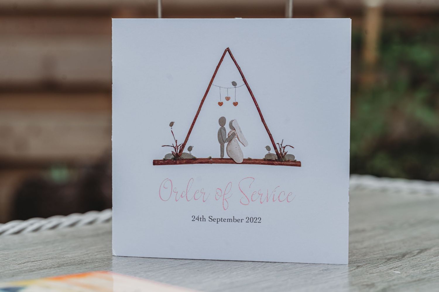 A minimalist wedding invitation card featuring silhouettes under a triangular arch with a simple date displayed below.