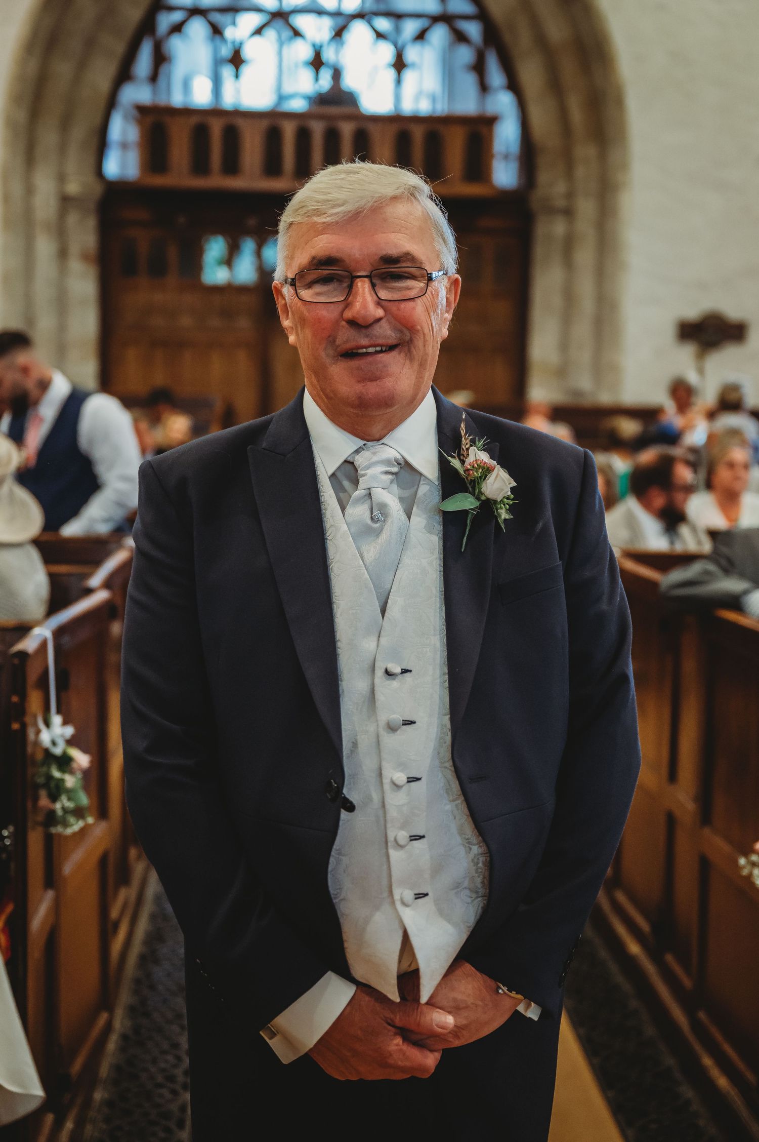 A person in formal wedding attire smiling in a church setting with traditional decor visible in background.