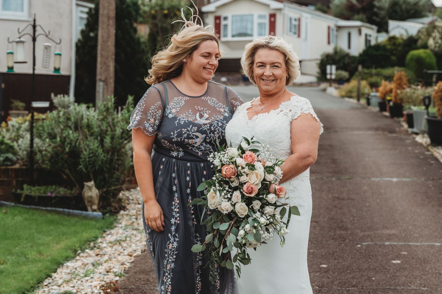 Two people stand together at a wedding event wearing a sparkly blue gown and white wedding dress holding floral bouquet.