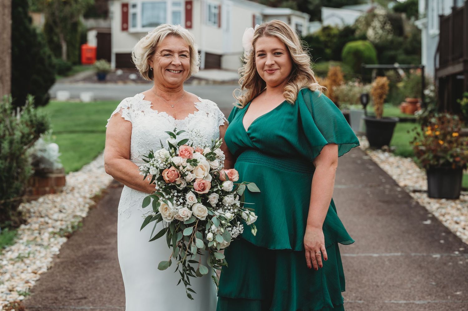 A beautiful outdoor wedding photo features a person in a white dress with floral bouquet and companion in emerald green.