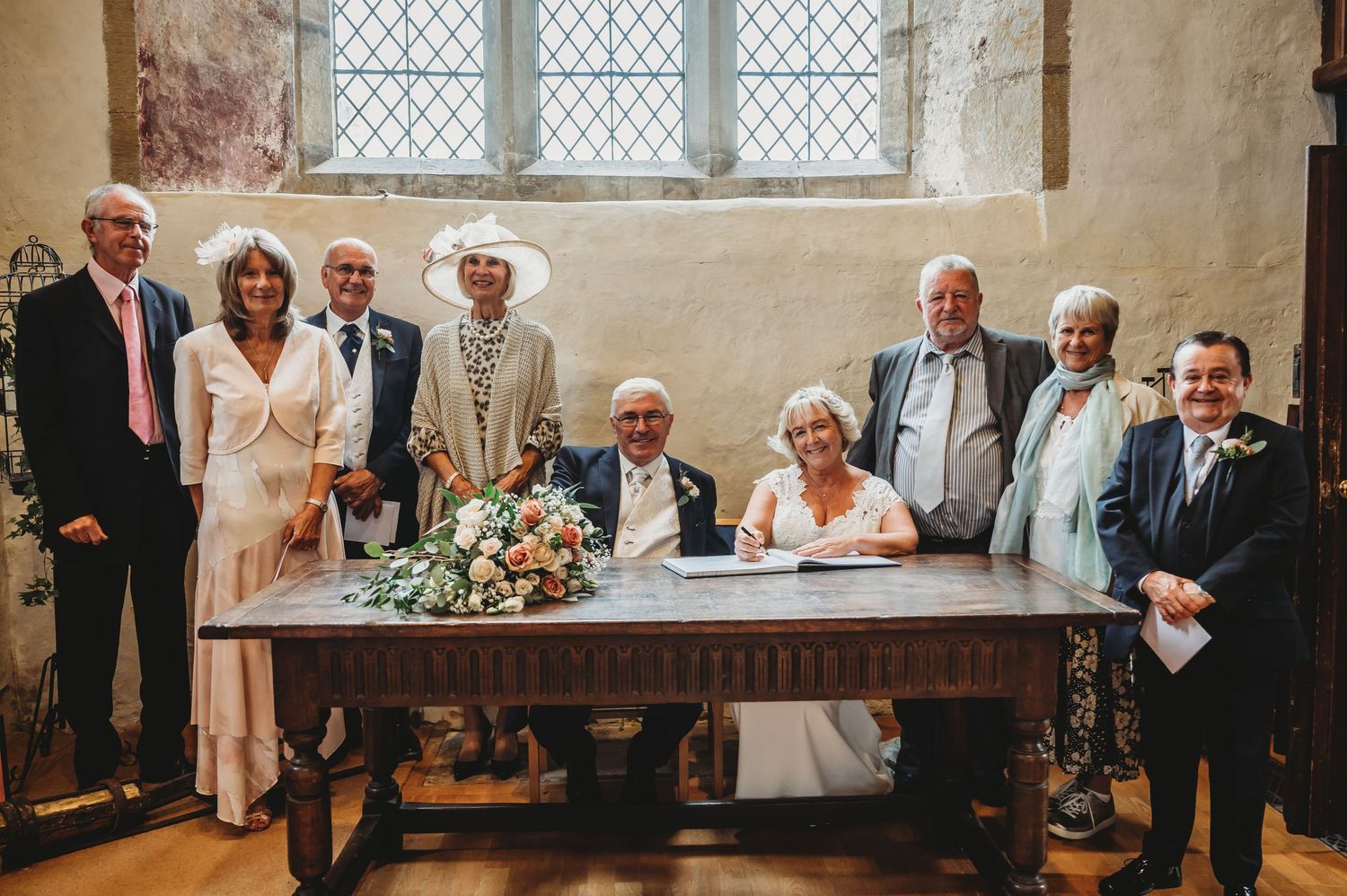 Group gathers around antique wooden table in historic church room with leaded glass windows for special occasion.