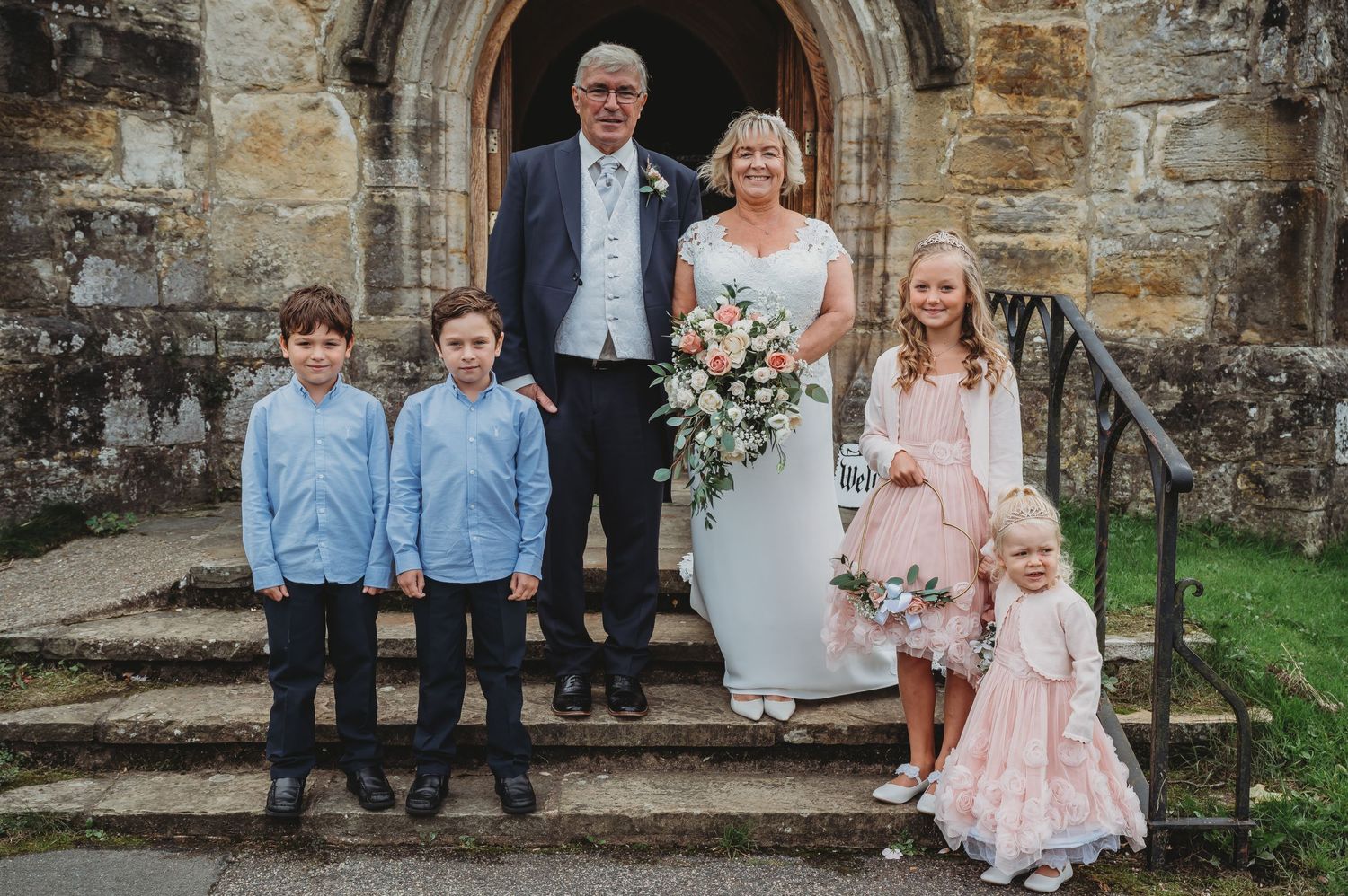 Family poses on old stone church steps for formal portrait on special day.