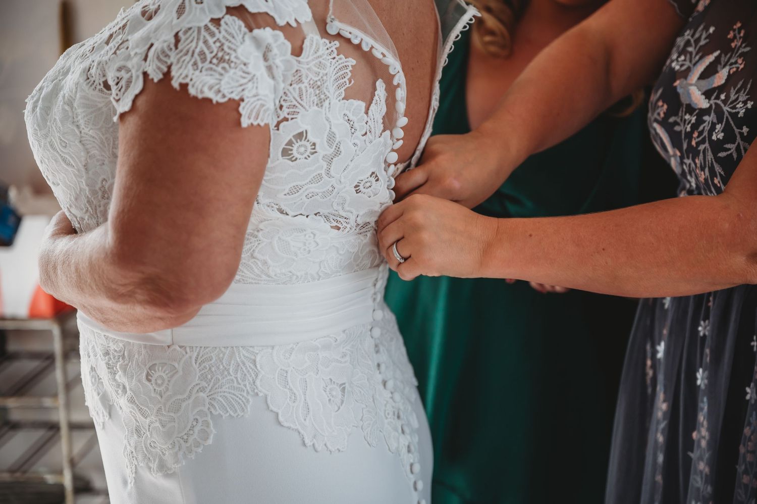 Close up of someone being helped into a white lace wedding dress with delicate cap sleeves.