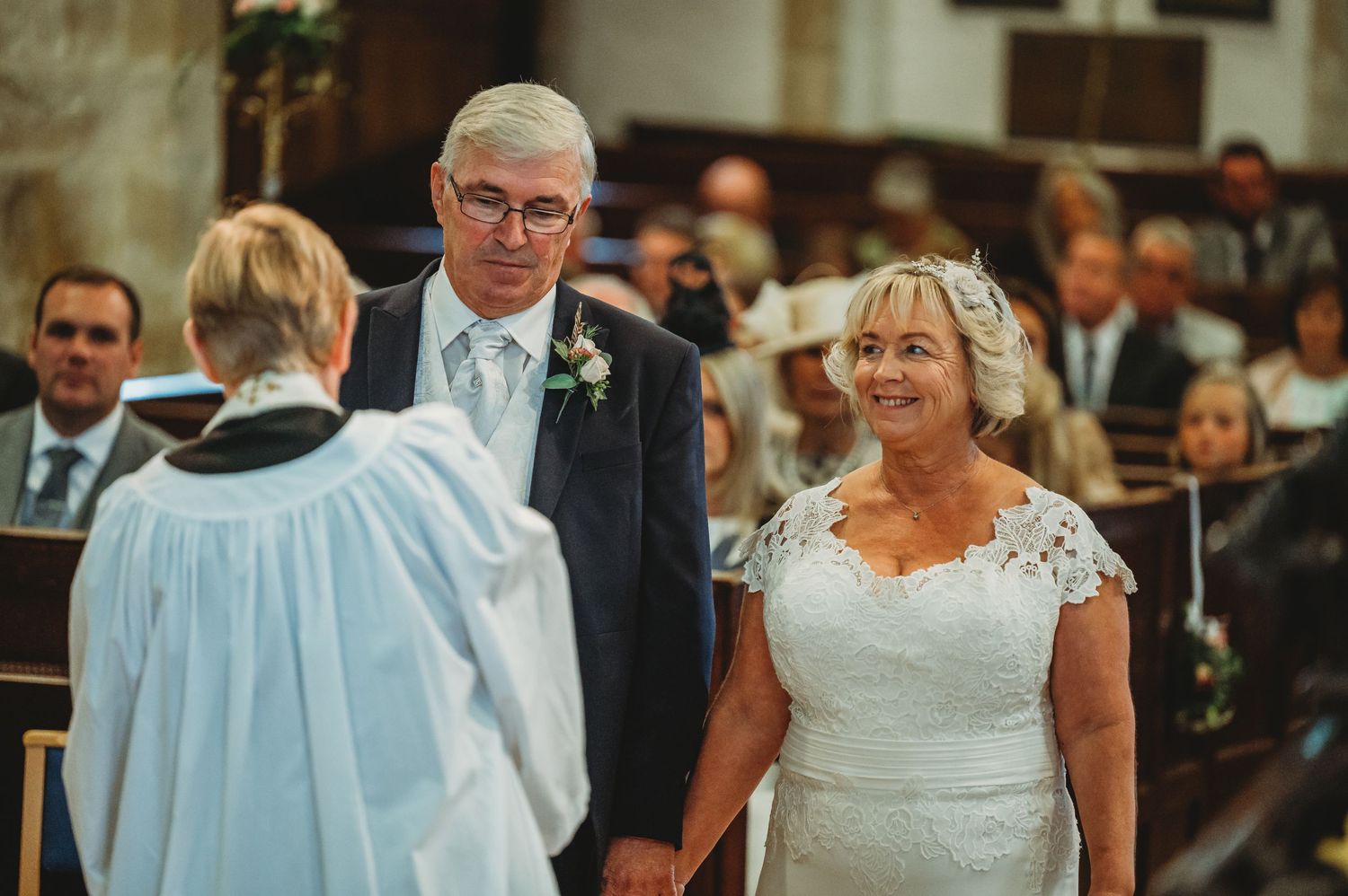 Traditional wedding ceremony in church with couple standing before minister in light blue robes during service.