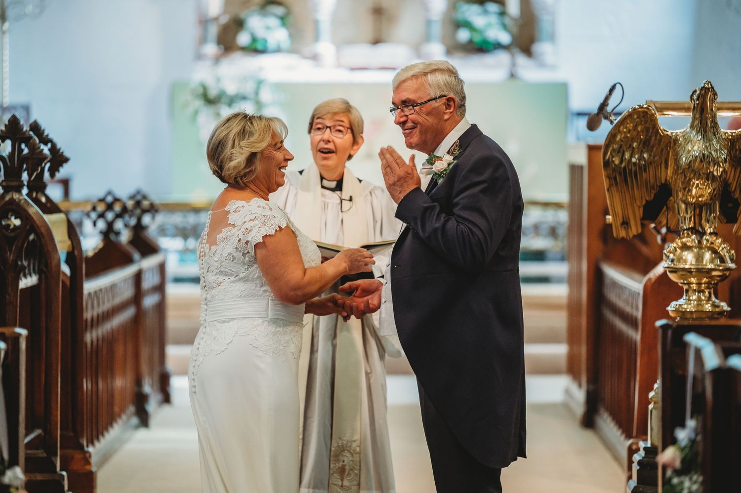 A wedding ceremony takes place inside a traditional church with ornate wooden pews and stained glass windows.