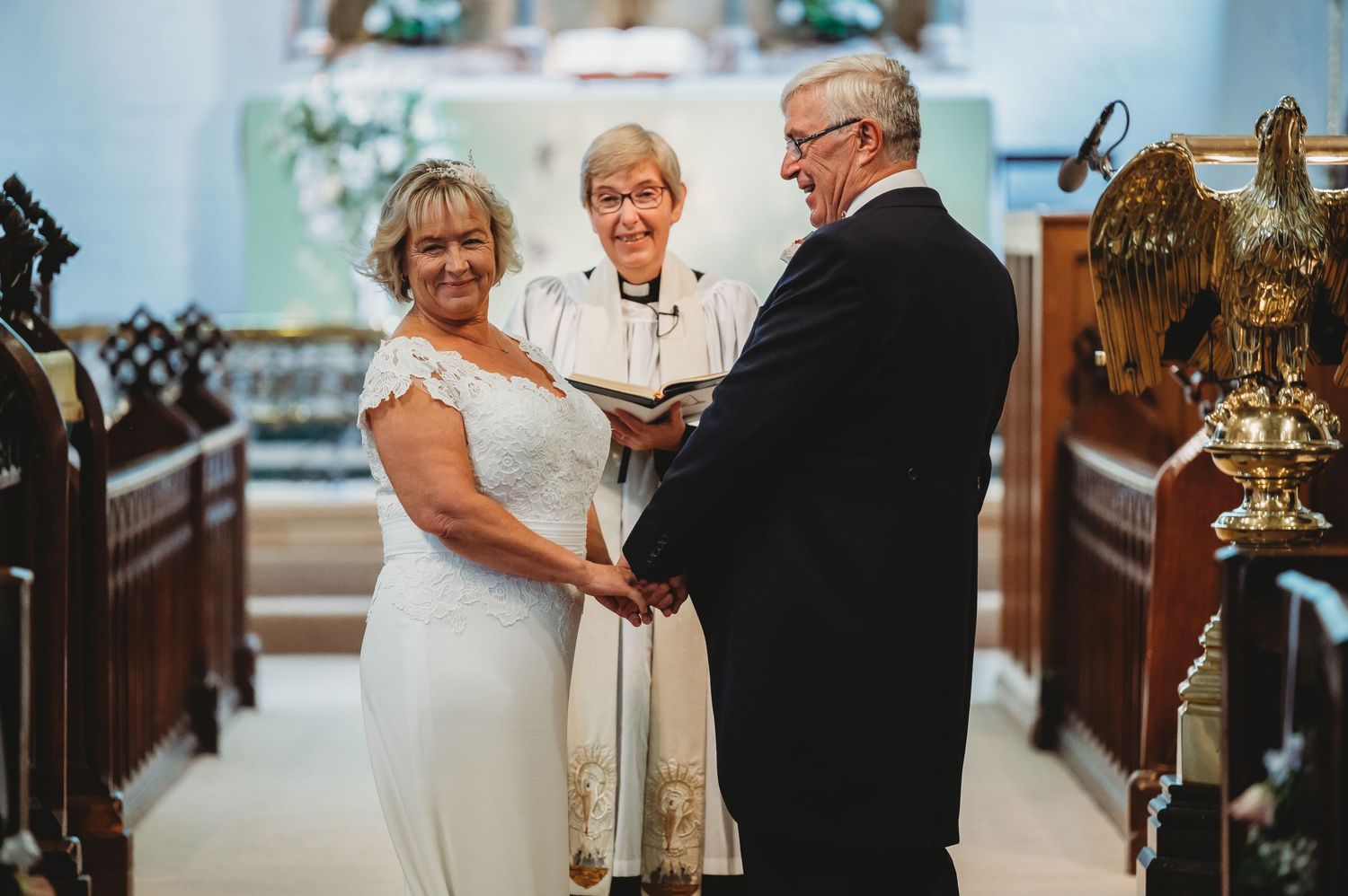 A couple joins hands during their wedding ceremony in a church with an officiant presiding over the service.