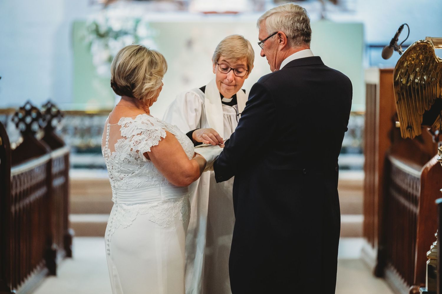 A couple exchanges wedding vows in a church ceremony while an officiant guides them through the sacred moment.