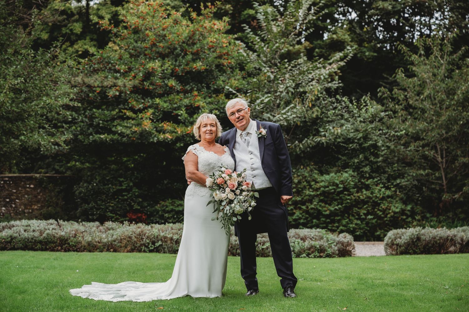 A happy couple shares a joyful moment together in a garden setting with lush greenery and elegant landscaping.