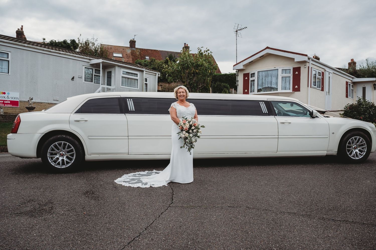 A white stretch limousine parked in a residential area with mobile homes in the background.