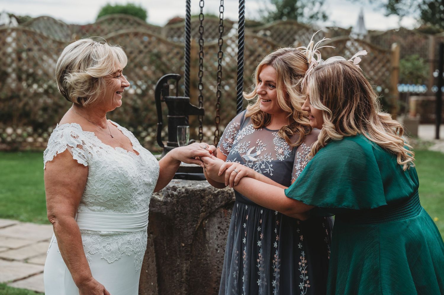 Wedding guests gather around a garden well to share celebratory drinks on a sunny afternoon.