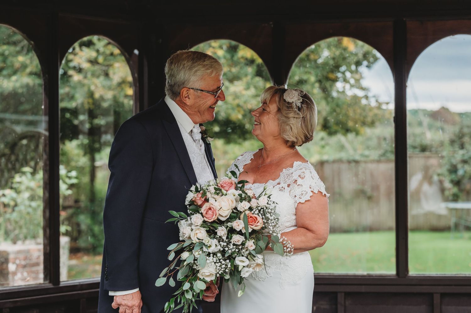 A couple shares an intimate moment in a gazebo, with the bride holding a beautiful white floral bouquet.
