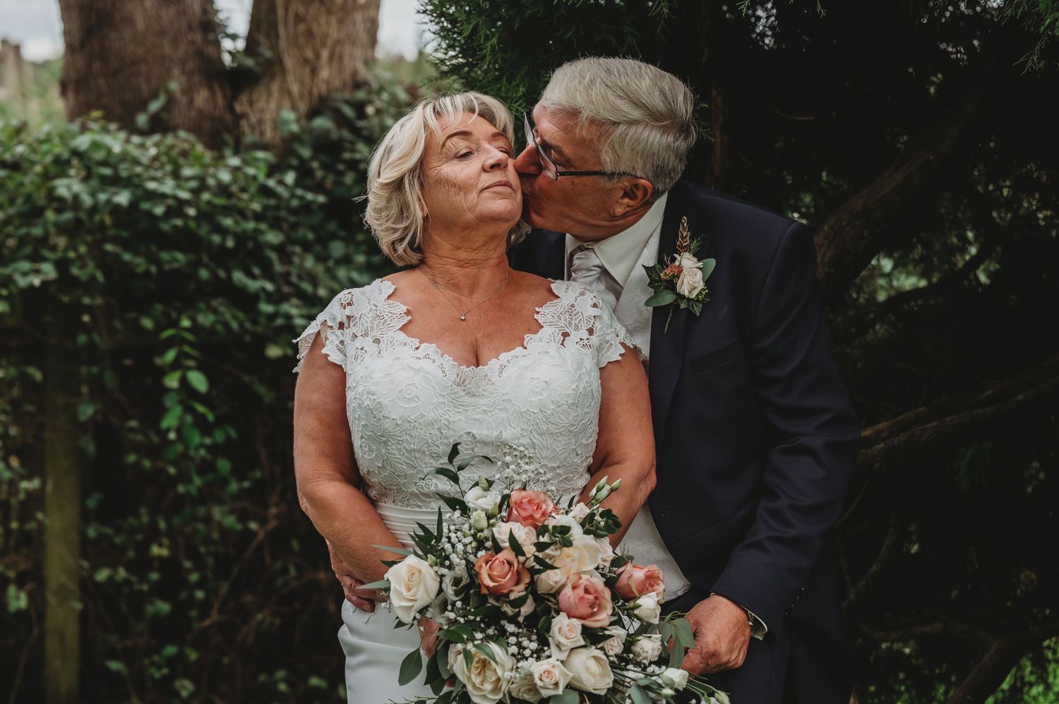 Elegant couple shares intimate moment during outdoor wedding ceremony with bride holding pink and white floral bouquet.