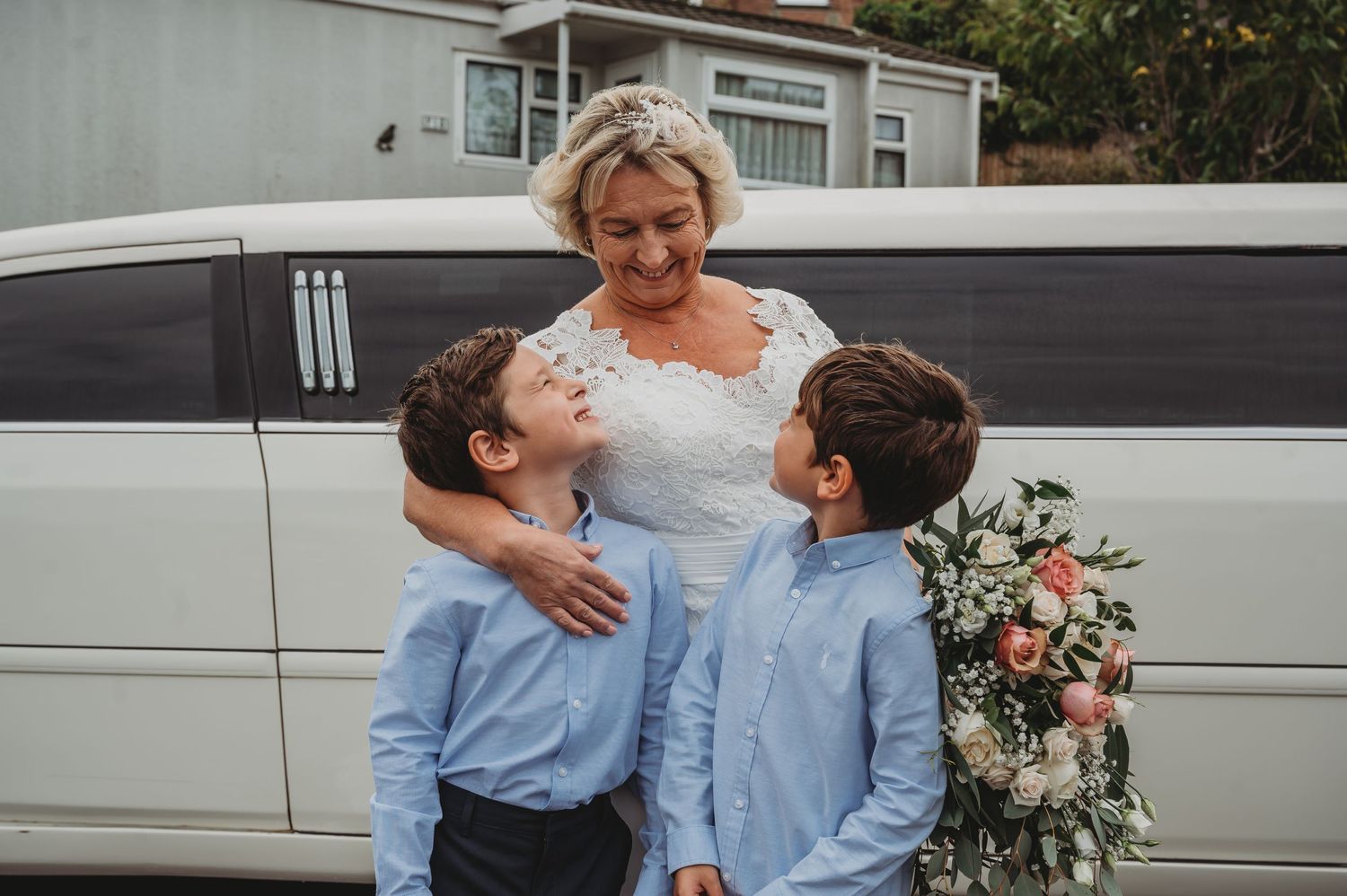 Candid moment outside limousine shows tender moment in light blue attire with floral bouquet.