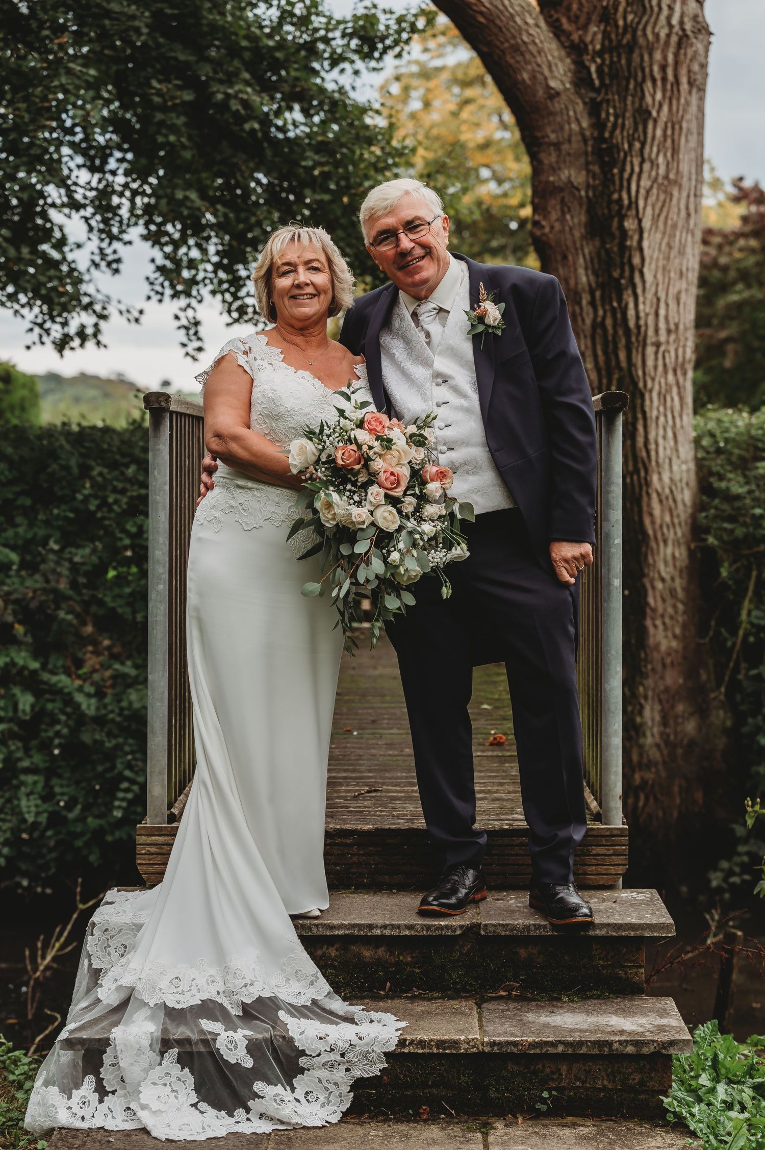 Newlywed couple stands on garden steps during autumn wedding, with bride holding lush pink and white bouquet.