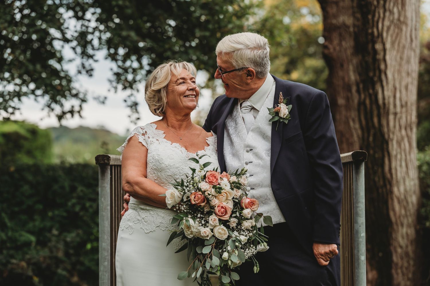 A tender outdoor wedding moment with a bouquet of coral and white flowers against a natural garden backdrop.