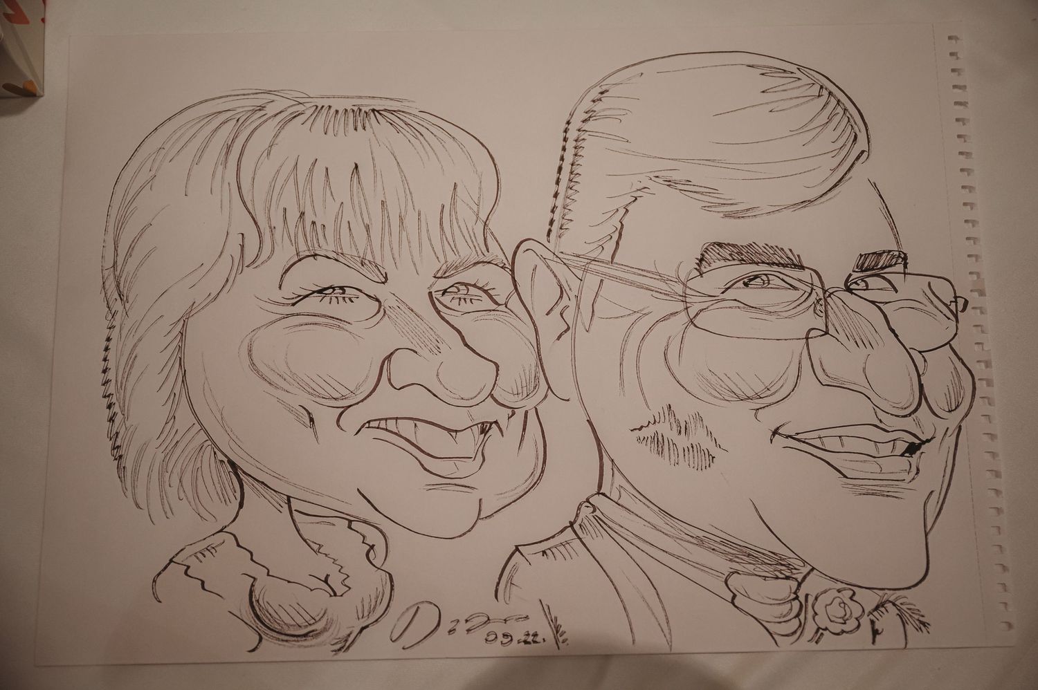 A pencil sketch showing two smiling caricature portraits drawn side by side on paper.
